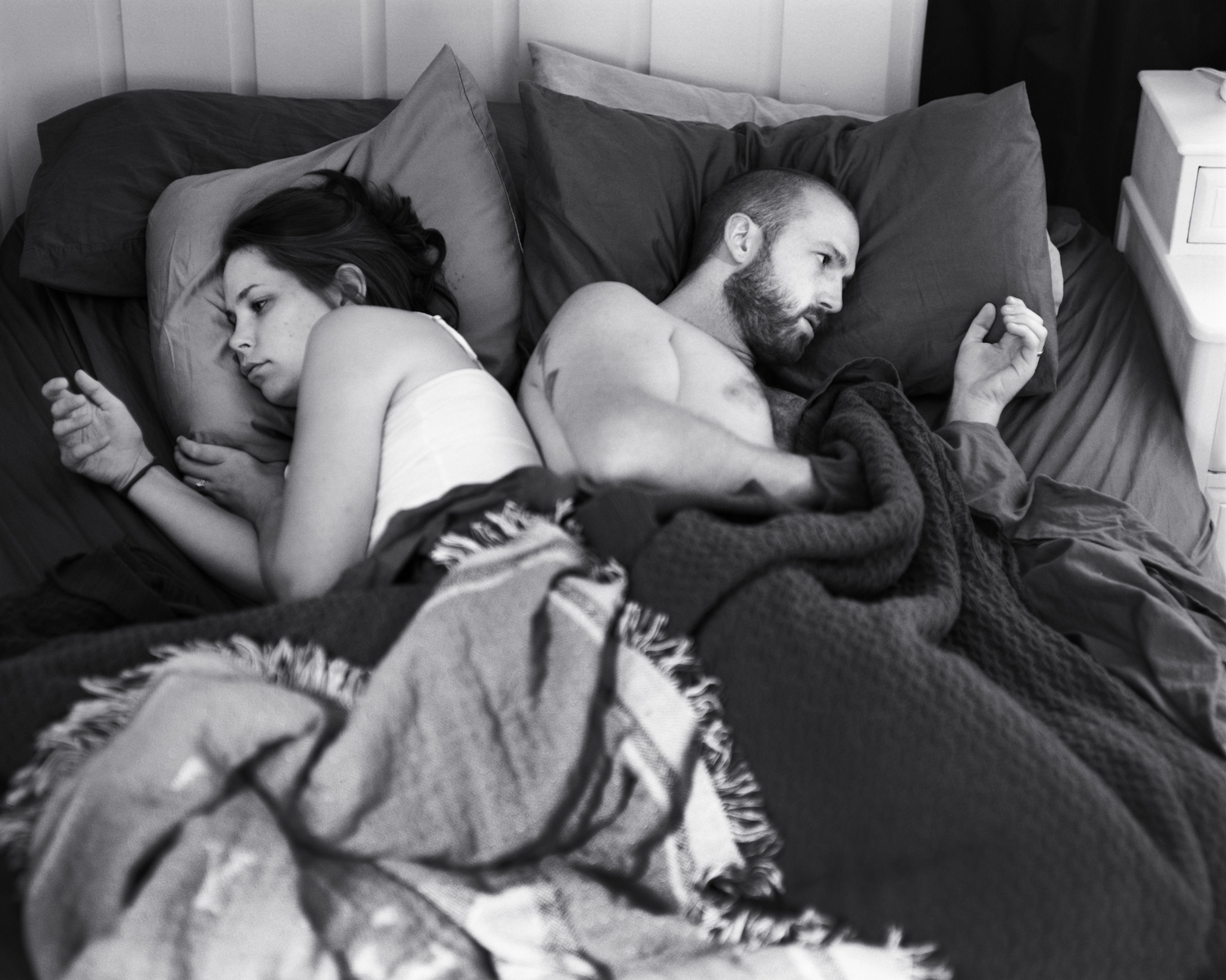Self portrait of the artist Eric Pickersgill and his wife Angie as they lay back to back while using thier non existant phones. The black and white portrait shows the young couple ignoring each other in bed.